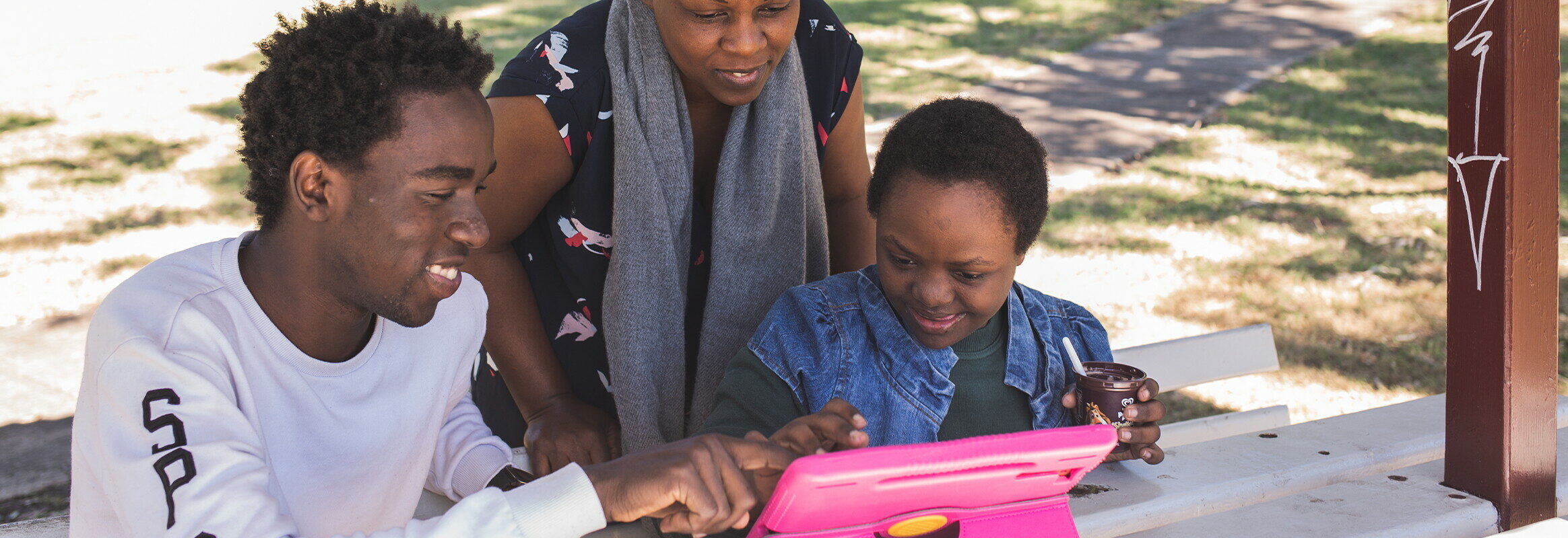 Woman, young man and child smiling and looking and pointing at iPad in a park