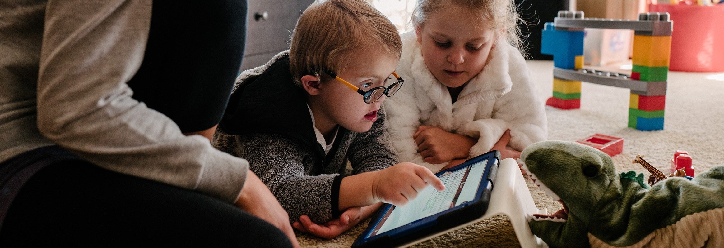 Jongetje tapt op pictogram in Proloquo2Go op iPad met zijn zus en moeder naast hem