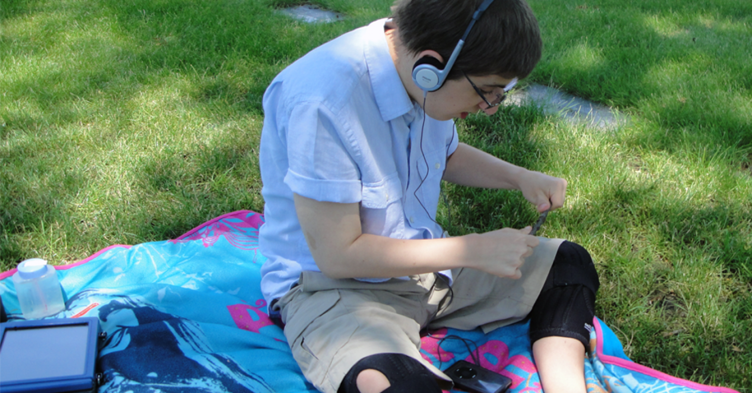 Boy in on grass field listening through headphones