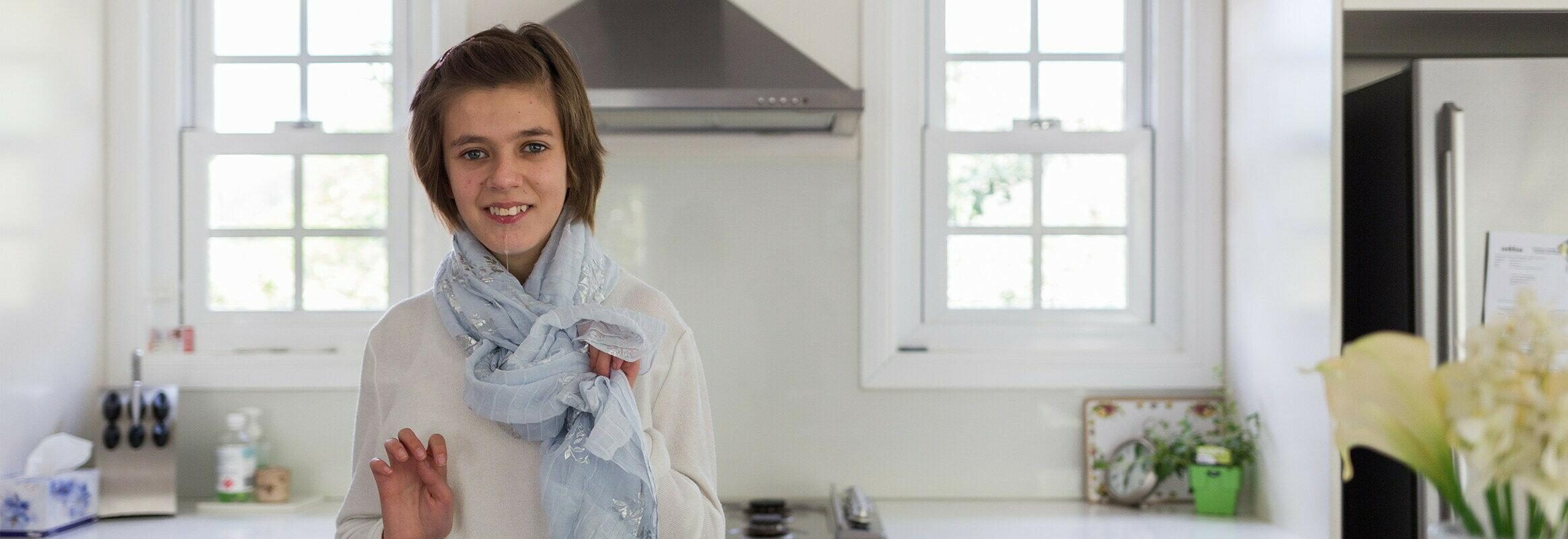 Lara, una joven blanca parada en una cocina luminosa, mirando a la cámara y sonriendo