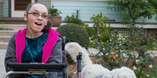 Elina, een witte vrouw in een rolstoel met een iPad en een hond aan haar zijde