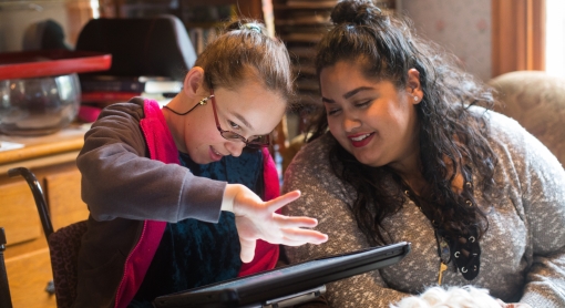 A girl is using an AAC device to communicate with an older woman