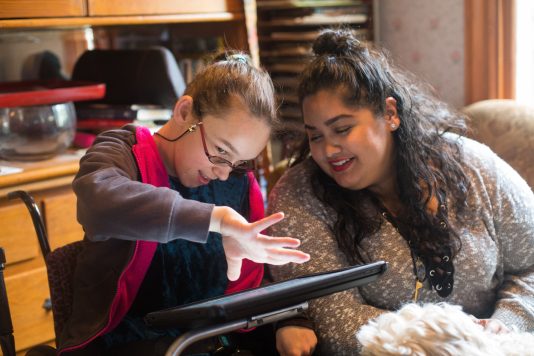 A girl is using an AAC device to communicate with an older woman