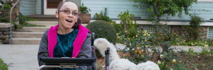 Elina, una mujer blanca en silla de ruedas con un iPad y un perro a su lado