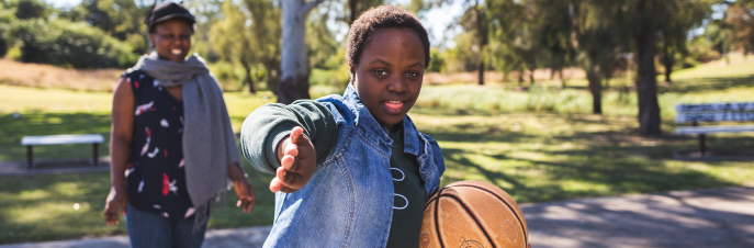 Bonita, a Malawian teenage girl on the basketball court, gesturing to the camera, with another black woman on the court in the background