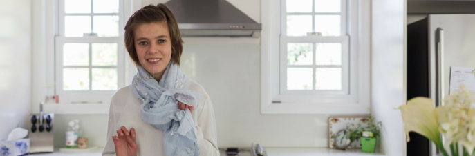 Lara, een jonge blanke vrouw in een lichte keuken, met uitzicht op de camera en glimlachend
