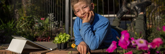 Tom, un adolescent blanc couché et travaillant dans le jardin avec un iPad à ses côtés