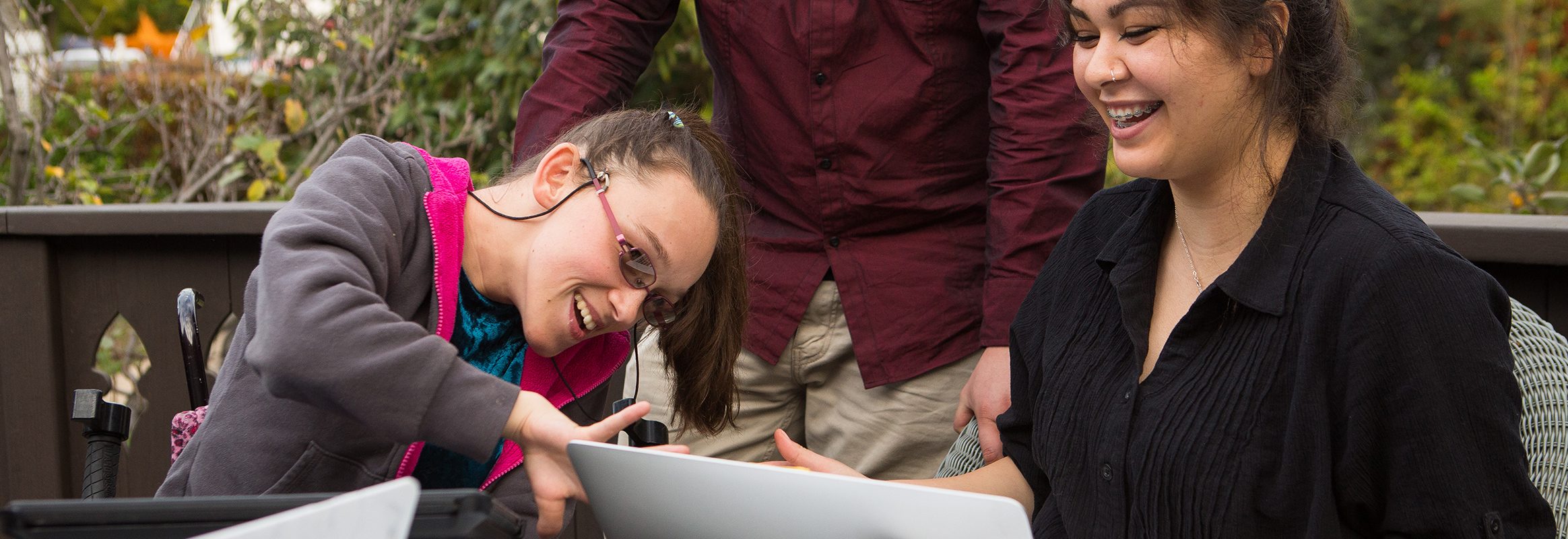 Drie mensen achter laptop, één gezicht verborgen, twee anderen glimlachen, wijzend en kijkend naar het scherm