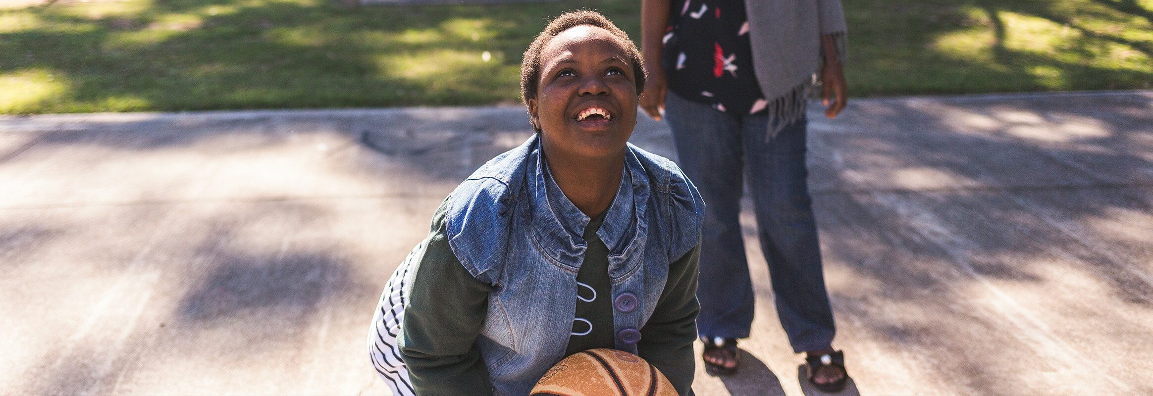 Girl looking up with basketball in her hands, ready to throw, adult in background