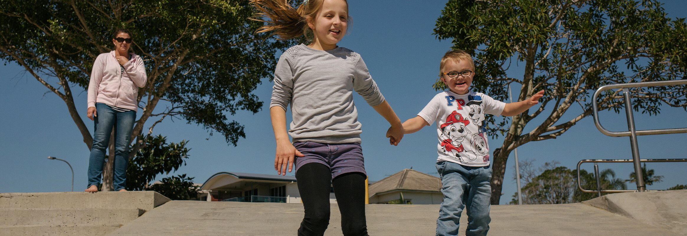 Twee kinderen lopen hand in hand over een helling terwijl hun moeder van een afstand toekijkt