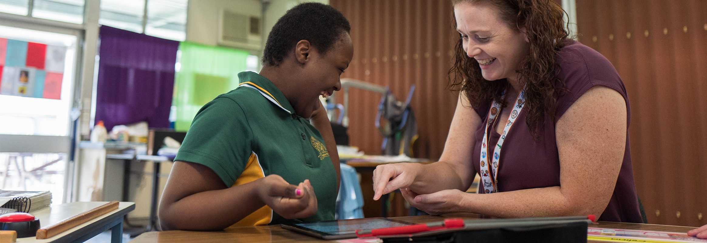 Teenage girl and teacher laughing communicating with AAC system Proloquo2Go