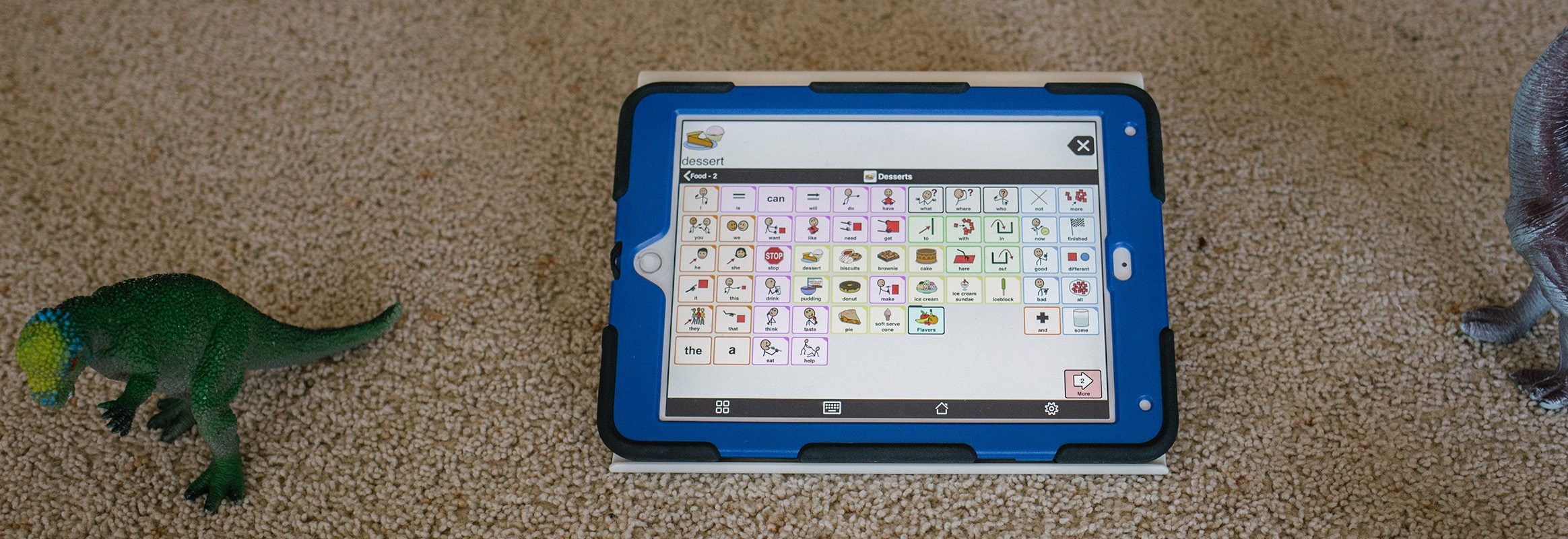 iPad with Proloquo2Go on carpet surrounded by toys