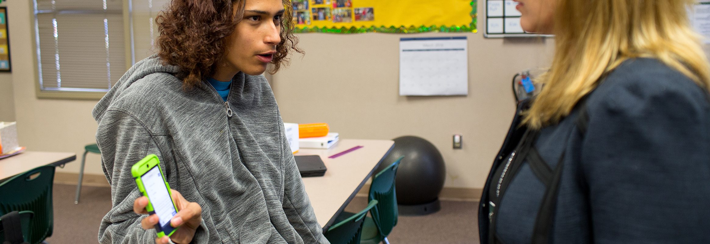 Teenager showing iPhone with text to teacher in classroom