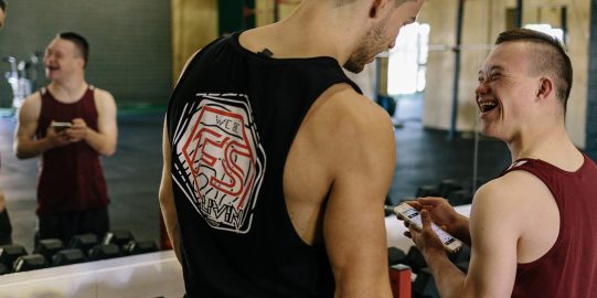 Two young men smiling and communicating with speech app in a gym