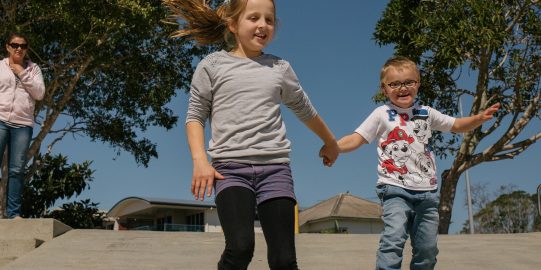 Dos niños caminando de la mano por una rampa mientras la madre observa desde la distancia