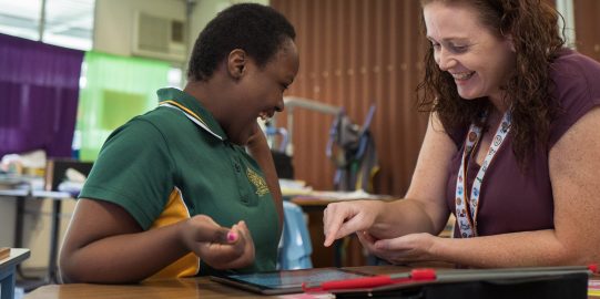 Teenage girl and teacher laughing communicating with AAC system Proloquo2Go