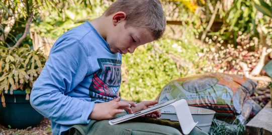 Young boy sitting outside using iPad