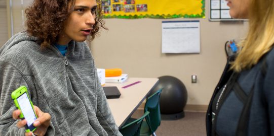 Teenager showing iPhone with text to teacher in classroom