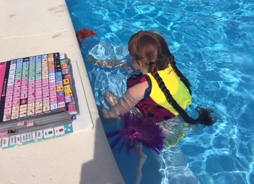 Ruby in a pool with an AAC book on the edge