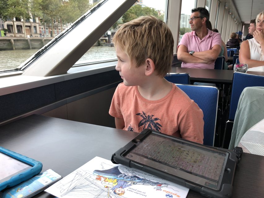 Hugo in a canal boat looking at the window, an iPad with Proloquo2Go on the table in front of him