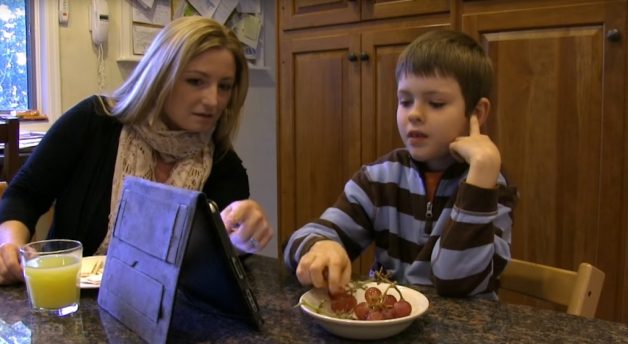 Moeder en zoon aan keukentafel, druiven etend en communiceren met iPad
