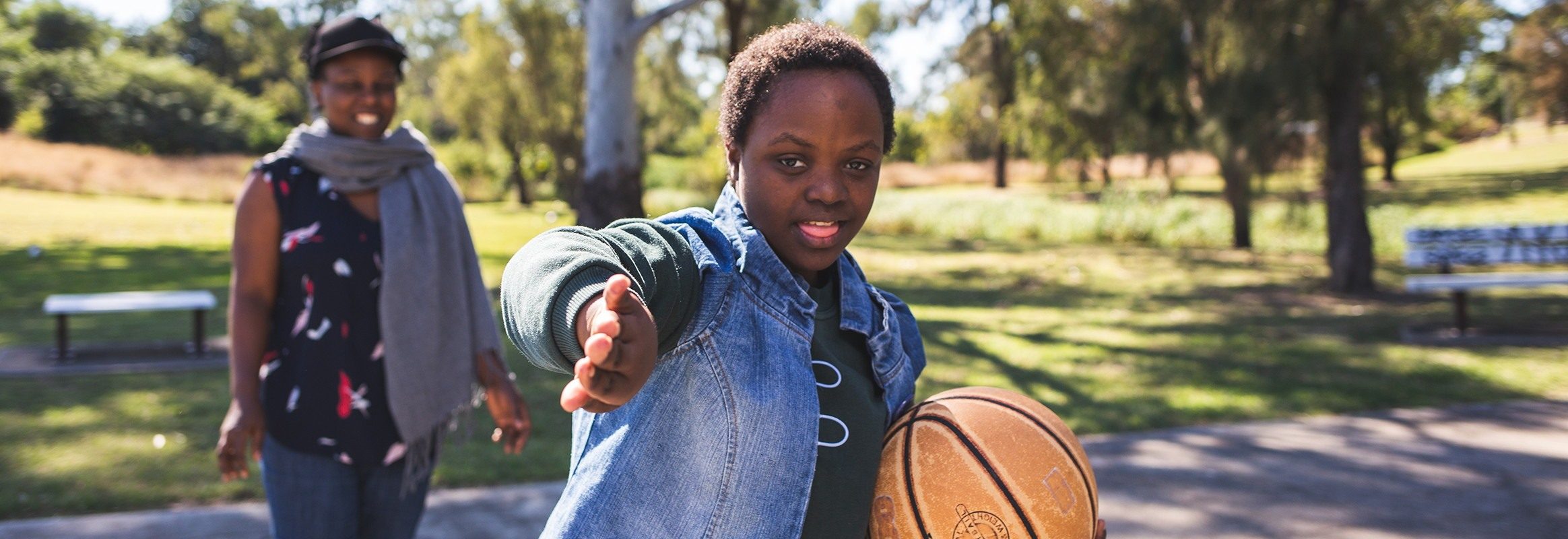 Bonita, een tienermeisje uit Malawi op het basketbalveld, gebarend naar de camera, met een andere zwarte vrouw op het veld op de achtergrond