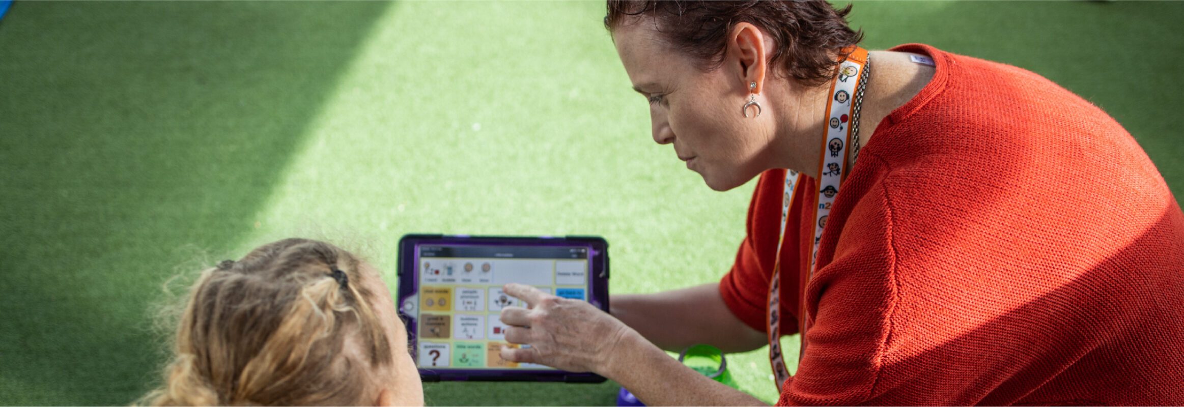 Amanda holding iPod and pointing to symbol on screen while young girl watches