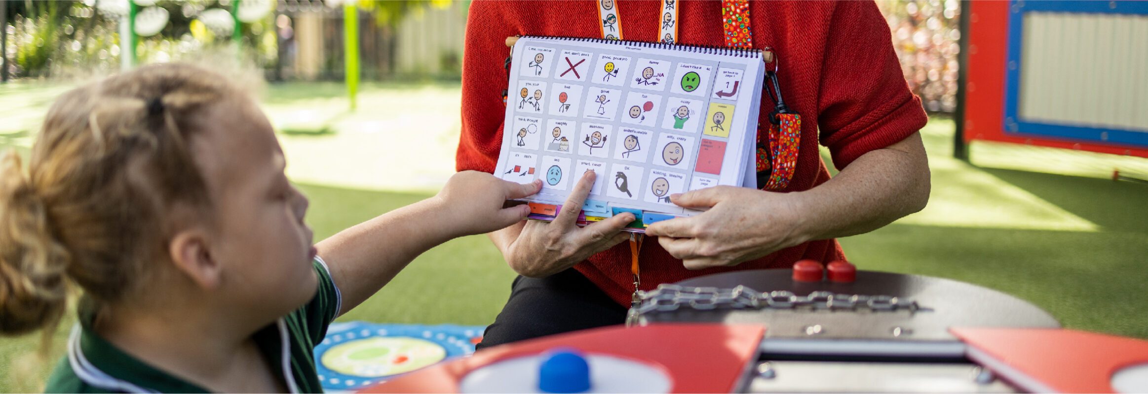 Girl pointing at symbol in PODD book while teacher holds the book