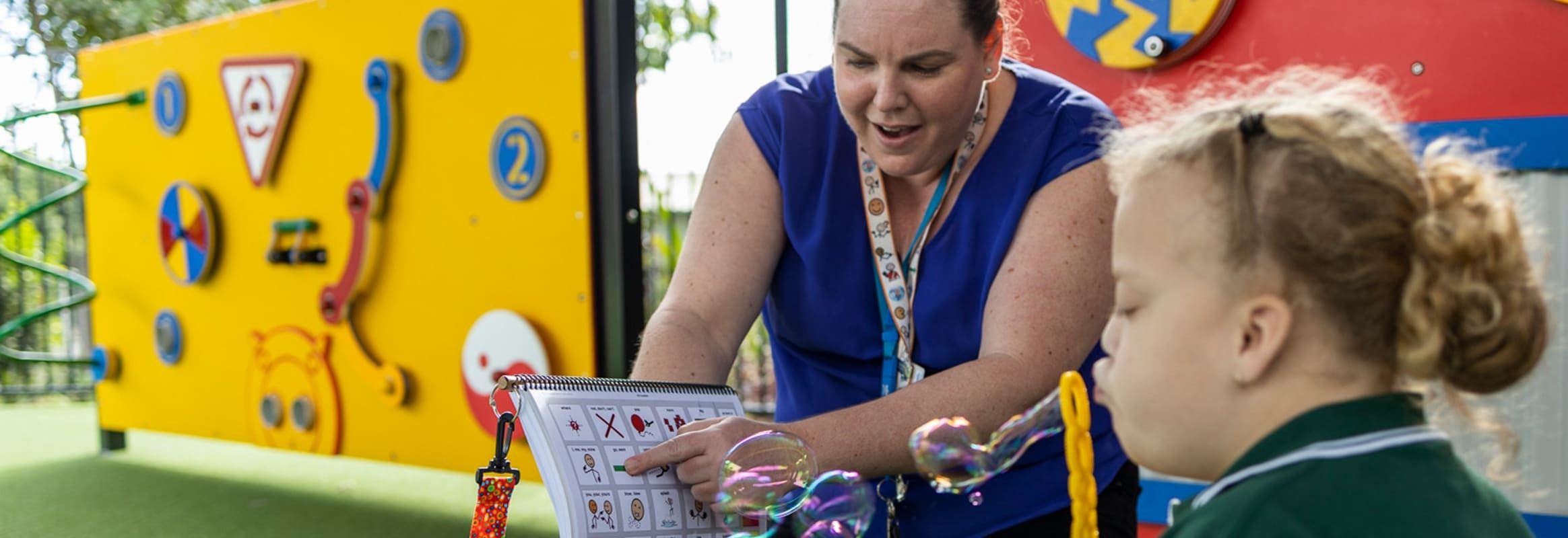 Girl blowing bubbles while woman points at printed PODD book