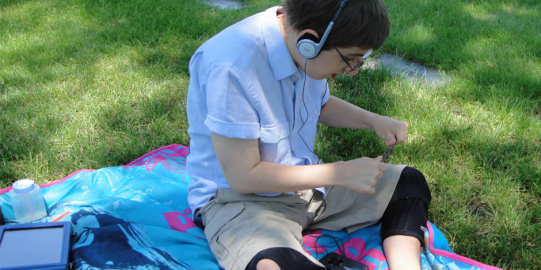 Boy in on grass field listening through headphones