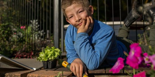 Tom, een witte tiener die in de tuin gaat liggen en werken met een iPad aan zijn zijde