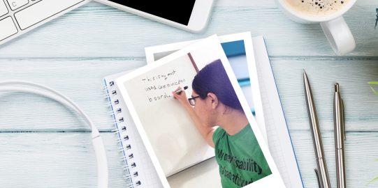 Keyboard, pen and notepad with photo of author Alyssa Hillary on table