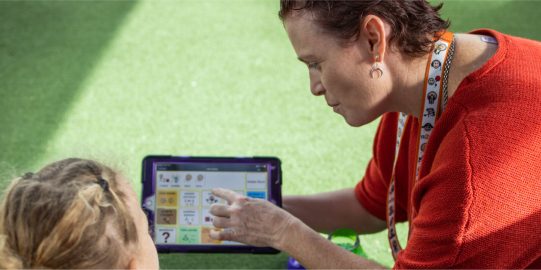 Amanda holding iPod and pointing to symbol on screen while young girl watches