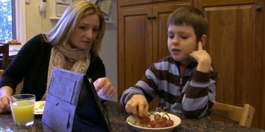 Mother child kitchen table eating grapes and talking using iPad