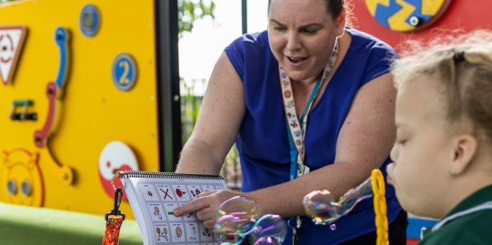 Girl blowing bubbles while woman points at printed PODD book