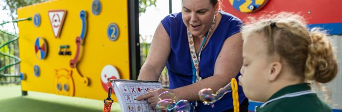 Girl blowing bubbles while woman points at printed PODD book